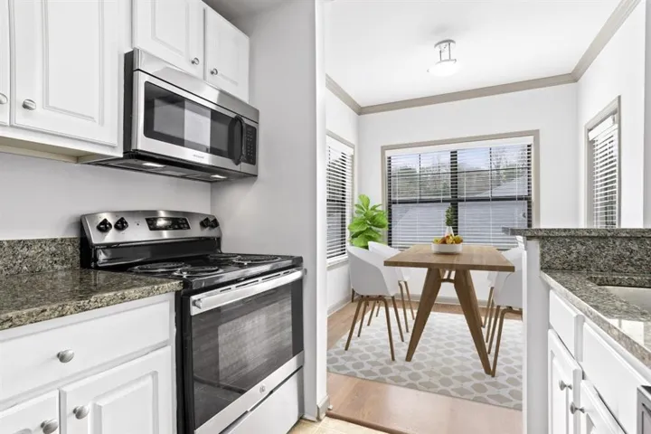 Kitchen with appliances with stainless steel finishes, light wood-type flooring, white cabinetry, crown molding, and dark stone countertops