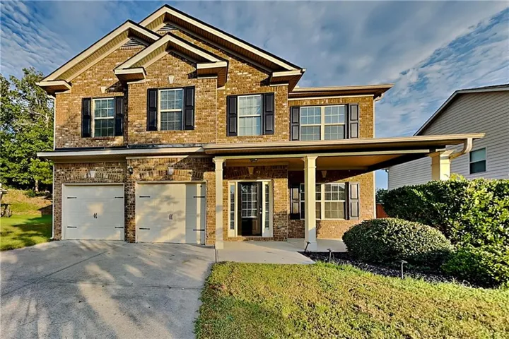 Brick exterior with two-car garage, covered entry porch, and traditional black louvered shutters