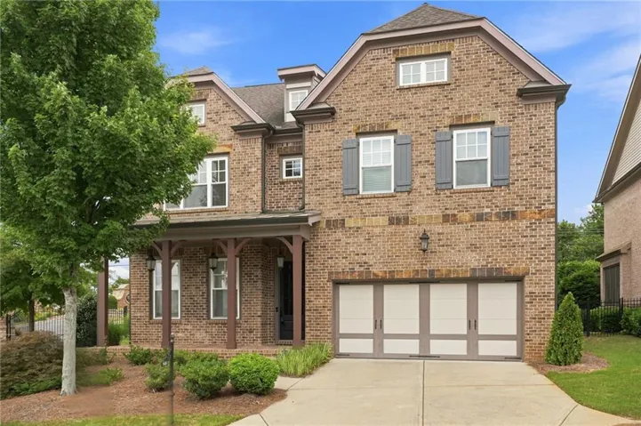 Brick facade residence featuring a covered front porch with decorative columns, a two-car garage, and multiple dormer windows