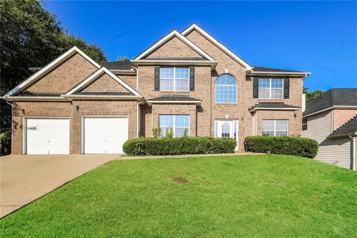 Brick exterior featuring a two-car garage, arched window, dark shutters, and a covered entryway
