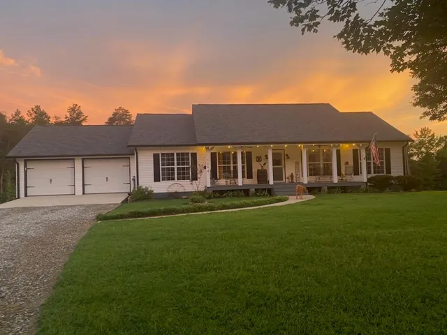 White exterior siding with dark shutters, covered front porch, attached two-car garage, and a gravel driveway