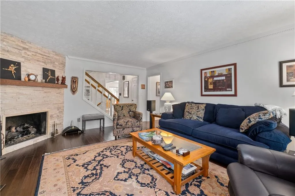 Living room featuring a stone fireplace, a textured ceiling, and dark wood-type flooring