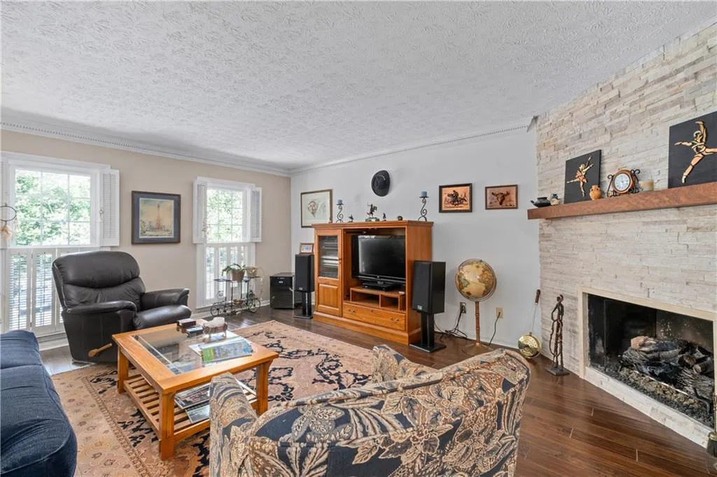 Living room with a stone fireplace, hardwood / wood-style flooring, ornamental molding, and a textured ceiling