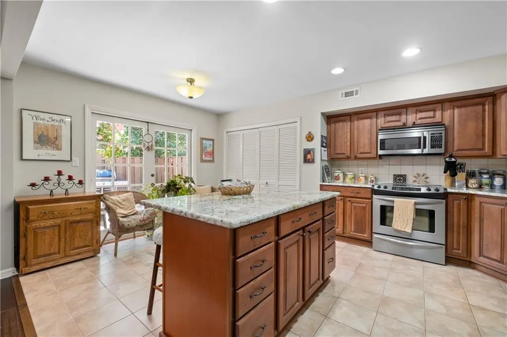 Kitchen featuring appliances with stainless steel finishes, backsplash, a kitchen island, and light tile floors