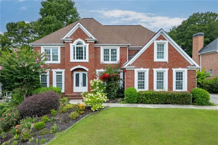 Brick exterior with white trim, arched dormer window, and mature landscaping