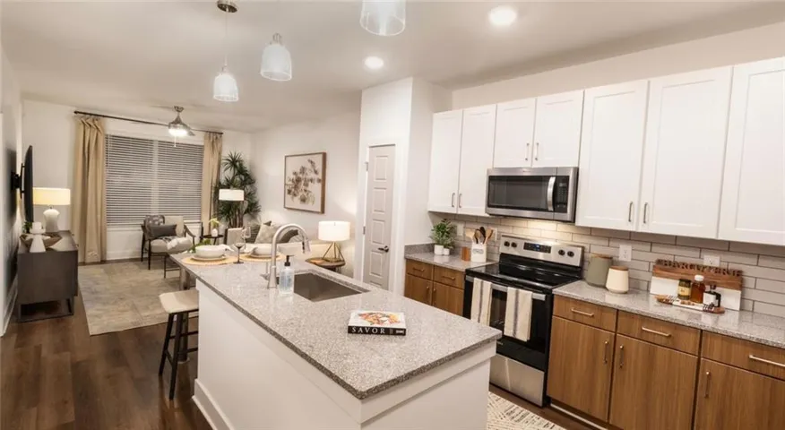 Kitchen featuring sink, dark hardwood / wood-style flooring, stainless steel appliances, and a center island with sink
