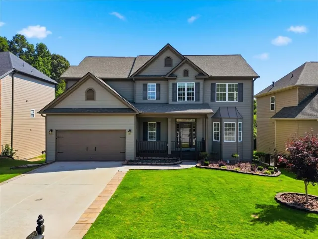 Two-story residence featuring a two-car garage, bay window, covered front porch, and established landscaping with mature trees