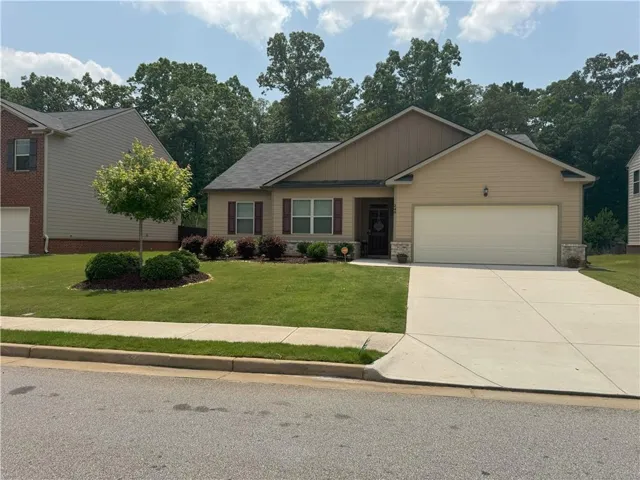 View of front of home featuring an attached garage, a front lawn, concrete driveway, and stone siding