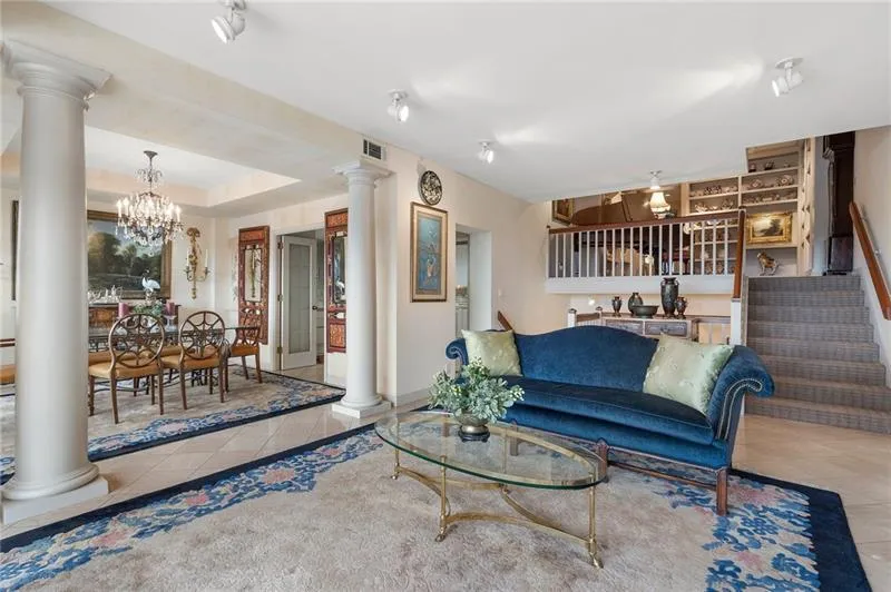 Tiled living room featuring decorative columns, visible vents, a raised ceiling, an inviting chandelier, and stairs