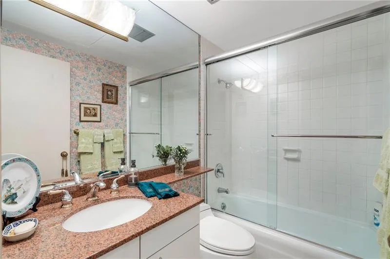 Full bath with enclosed tub / shower combo, vanity, toilet, and wallpapered walls