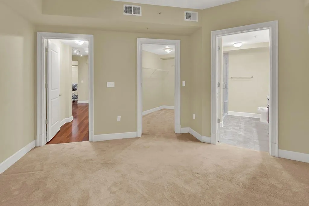 Unfurnished bedroom with light carpet, ensuite bath, a walk in closet, and a closet