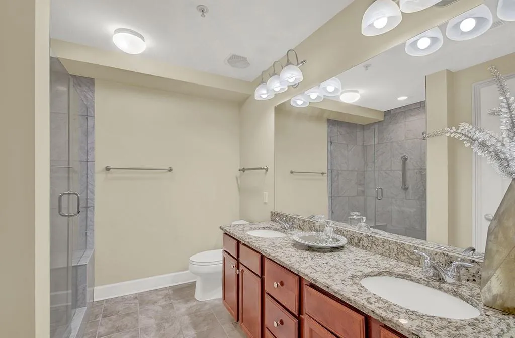 Bathroom featuring toilet, double vanity, tile flooring, and an enclosed shower