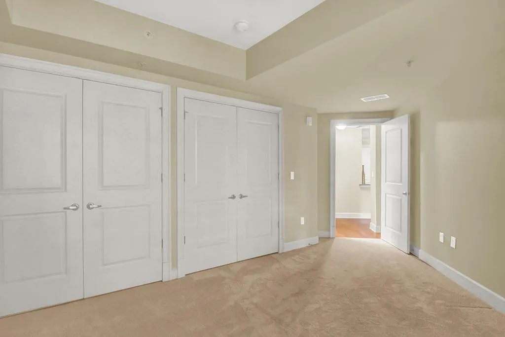 Unfurnished bedroom featuring a tray ceiling, multiple closets, and light colored carpet
