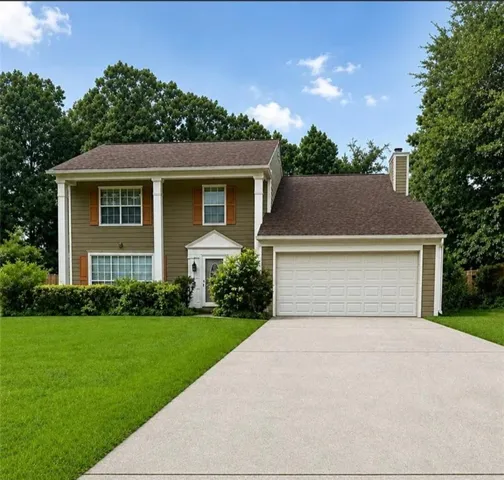 Two-story home featuring a broad driveway, attached two-car garage, and established landscaping