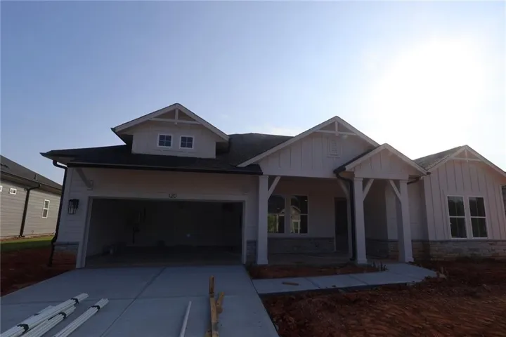 Contemporary single-story residence featuring a two-car garage, board and batten siding, stone veneer accents, and a covered front porch with substantial columns