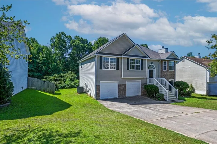 Split-level residence featuring a gray siding exterior with stone accents, a two-car garage, and a concrete driveway