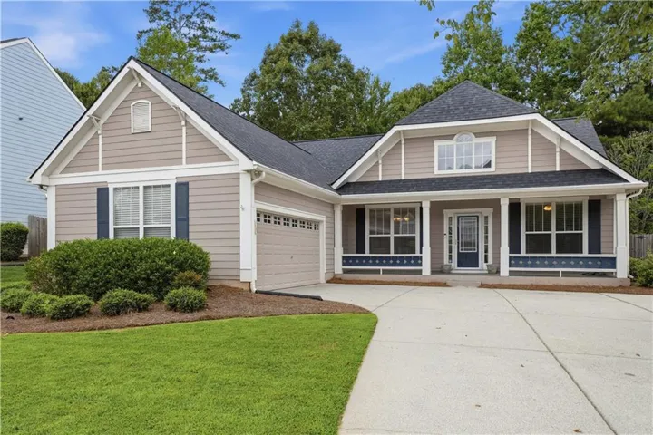 Two-car garage, covered entry, front porch with decorative trim, arched window on second level, and mature landscaping