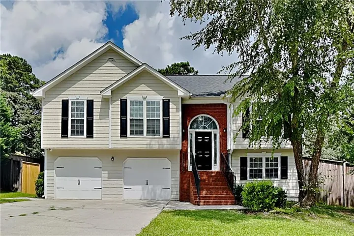 Two-story exterior with light-colored siding, brick accents, dual garage doors, a covered entry, and a mature tree