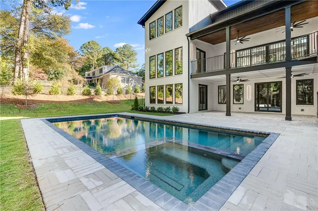 Back of property with ceiling fan, a patio, a pool with connected hot tub, and a balcony