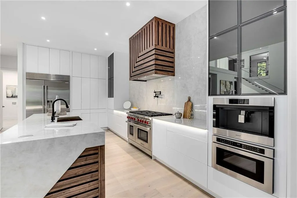 Kitchen with light stone counters, modern cabinets, high quality appliances, light wood-style flooring, and white cabinetry
