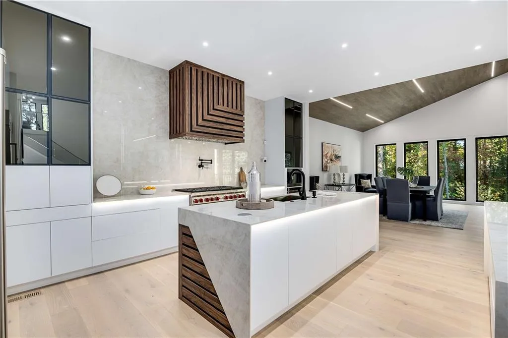 Kitchen featuring modern cabinets, light wood-type flooring, an island with sink, light stone counters, and decorative backsplash