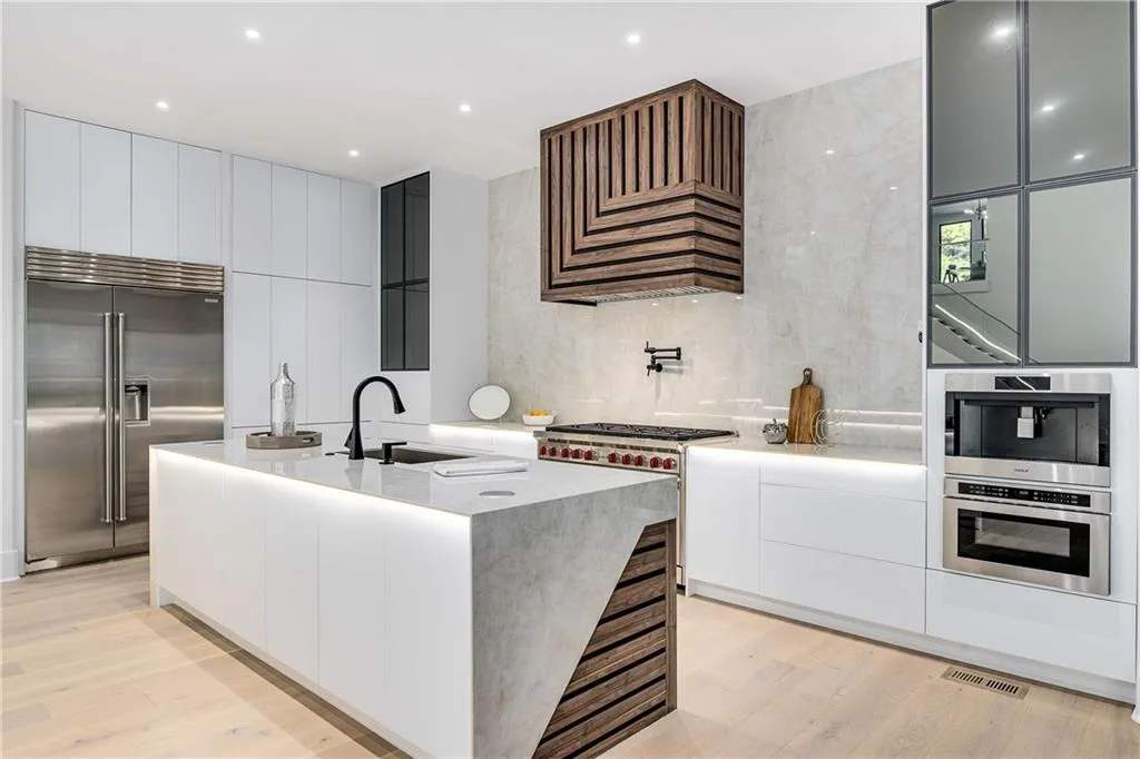 Two tone kitchen featuring high quality appliances, modern cabinets, a center island with sink, light stone counters, and light wood-style flooring