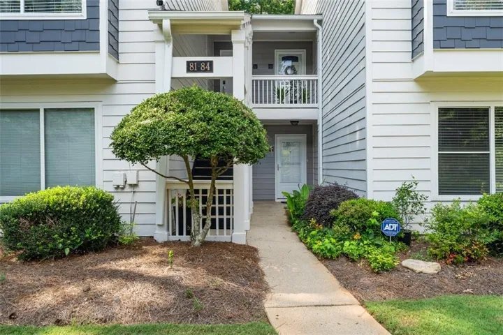 Property entrance with a concrete walkway, mature landscaping, and a second-story balcony with white railings