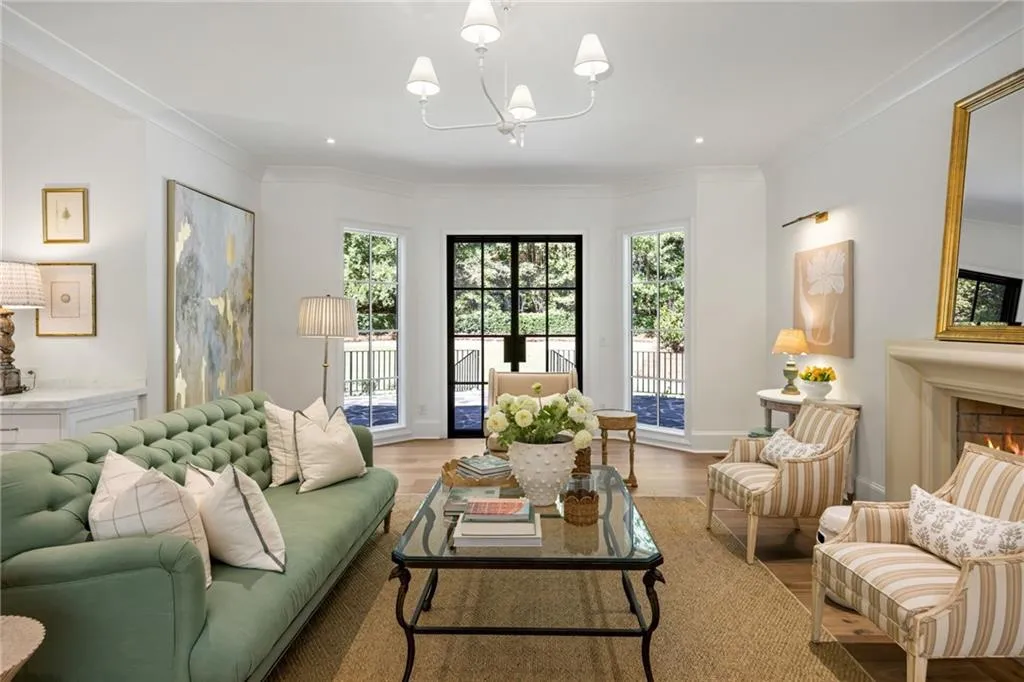 Living area featuring a masonry fireplace, tall multi-pane windows, black-framed French doors, crown molding, and a tiered chandelier