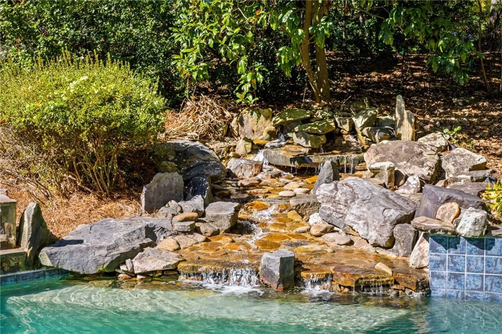 Natural stone waterfall feature with tiered rock formations, integrated stone basin, and blue tile trim