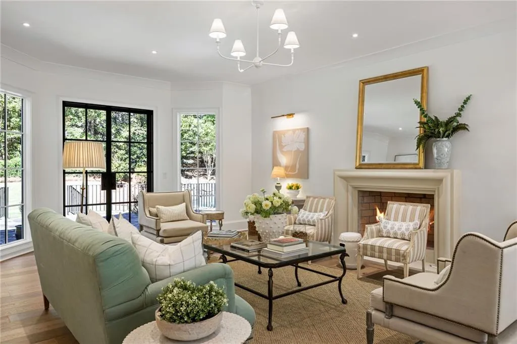 Living area featuring wood-finish flooring, a traditional stone fireplace mantel, black-framed French doors, multi-pane windows, and a central chandelier