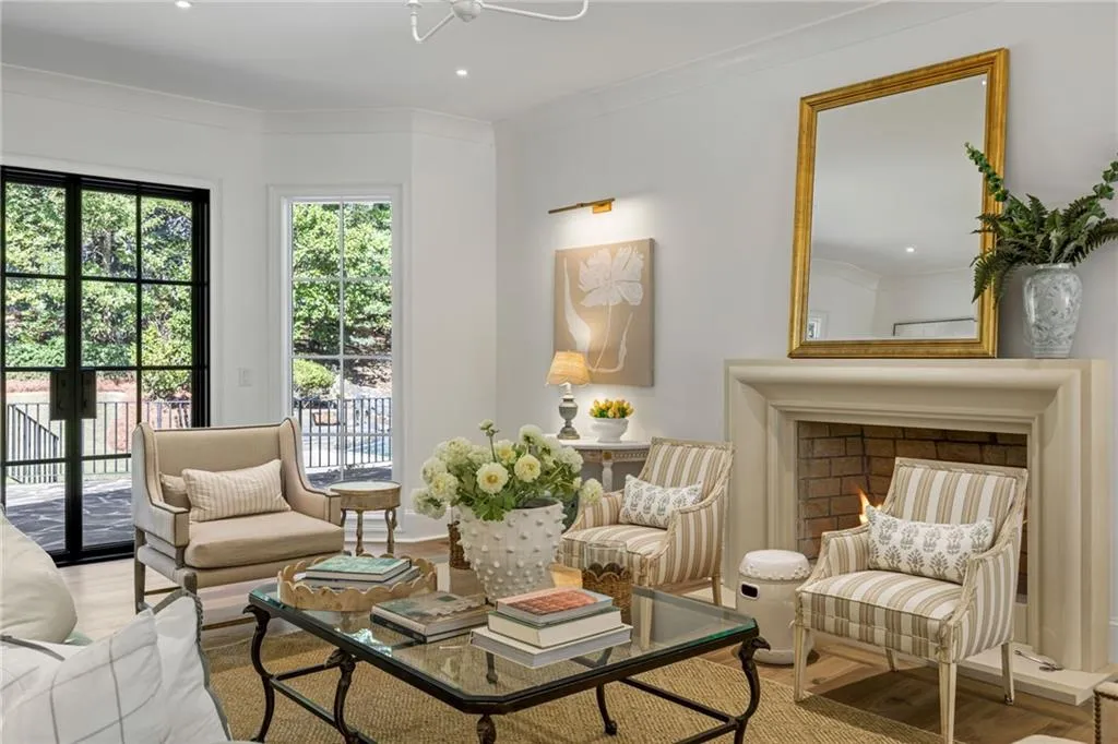 Light-filled room featuring large, black-framed steel doors, wood-finish flooring, a traditional stone fireplace mantel, and recessed ceiling lighting
