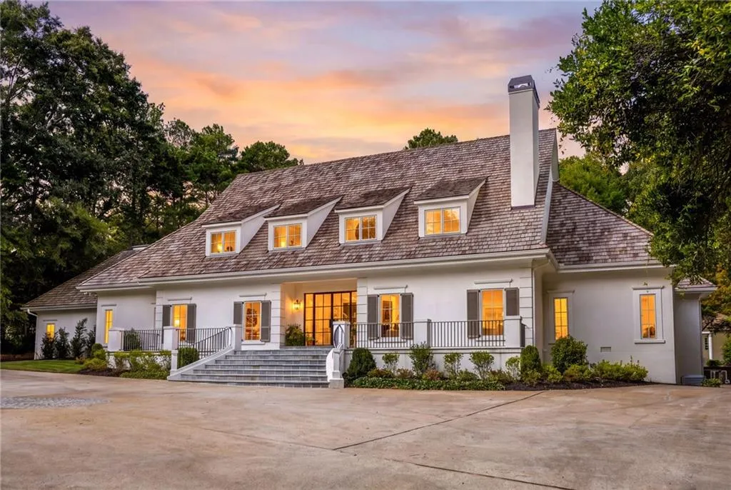 Traditional exterior featuring a wood-shake roof, dormer windows, white stucco facade, metal railing, and a raised stone staircase