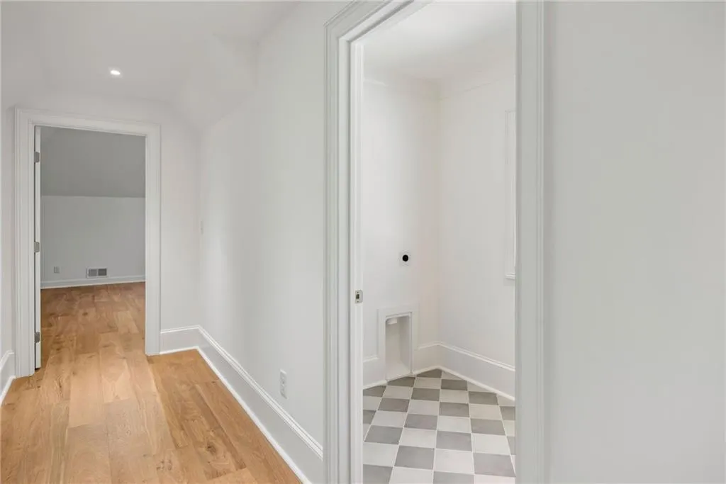 Hallway featuring wood-finish flooring and recessed lighting, with an entry to a room showcasing checkerboard tile flooring and built-in utility hookups
