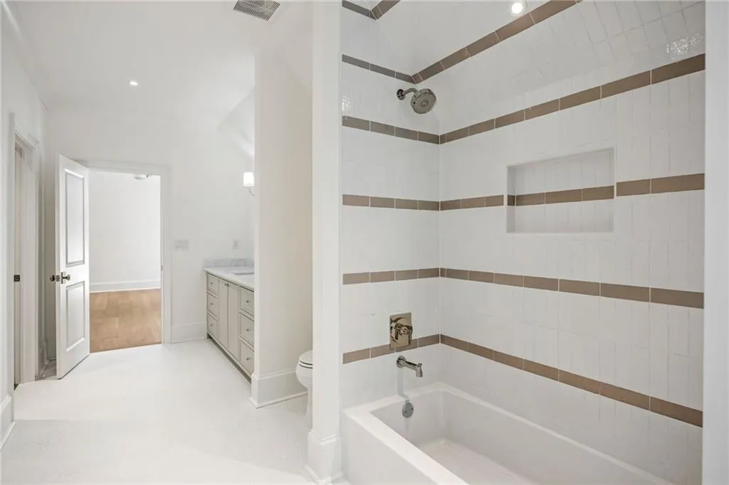 Bathroom featuring a tub-shower combination with horizontal tile accents and a built-in recessed wall niche, chrome plumbing fixtures, and a vanity cabinet with a stone countertop