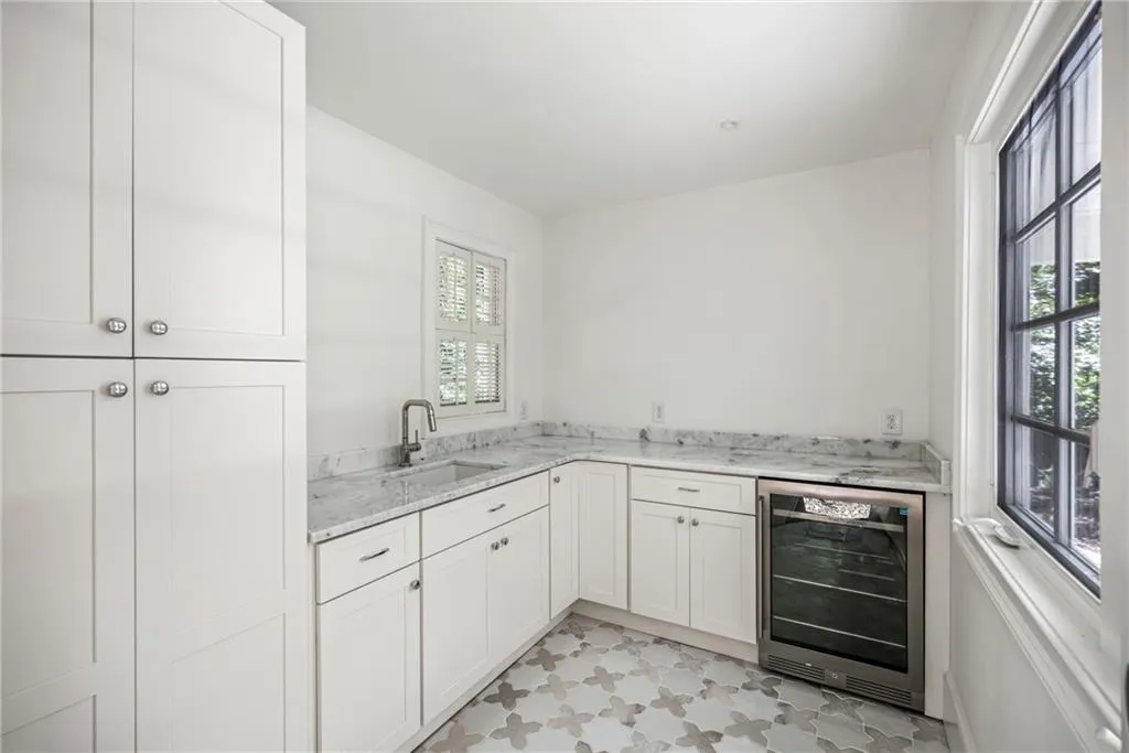 Custom cabinetry, stone-finish countertops, integrated wine refrigeration, under-mount sink with metal faucet, and patterned tile flooring