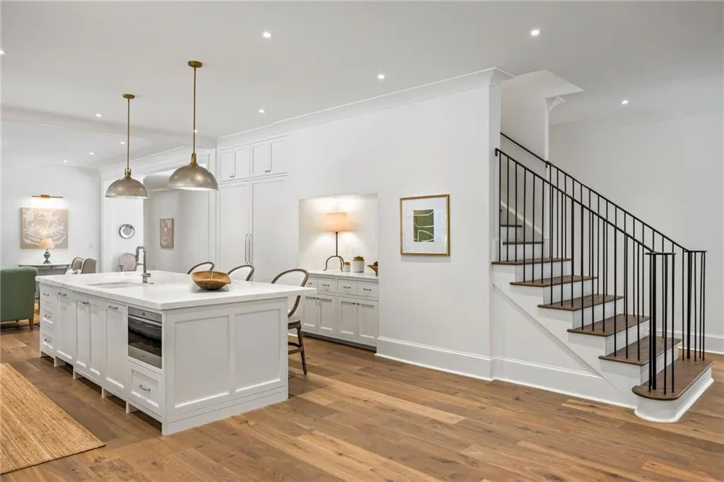 Kitchen island with stone countertop, wood-finish flooring, custom built-in cabinetry, recessed lighting, and metal staircase railing