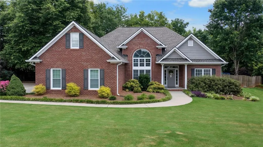 Brick exterior with gray siding accents, arched transom window, covered entry, curved concrete walkway, and landscaped garden beds