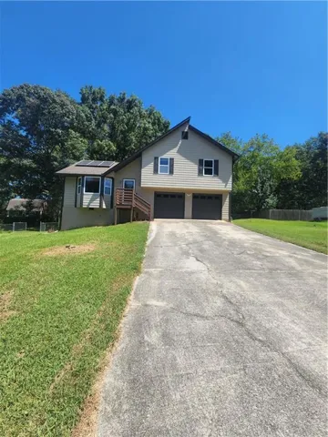 Two-car garage with individual doors, wood-finish exterior stairs, and a multi-level structure with a bay window