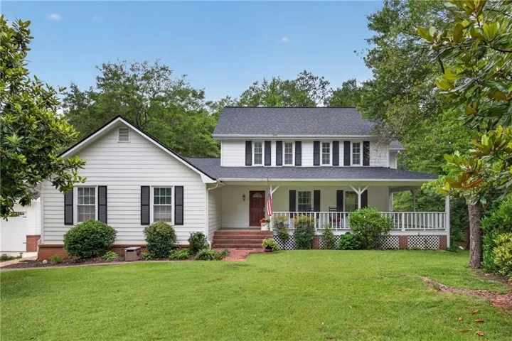 Two-story white siding residence featuring a covered front porch with white railing, contrasting black shutters, and an asphalt shingle roof