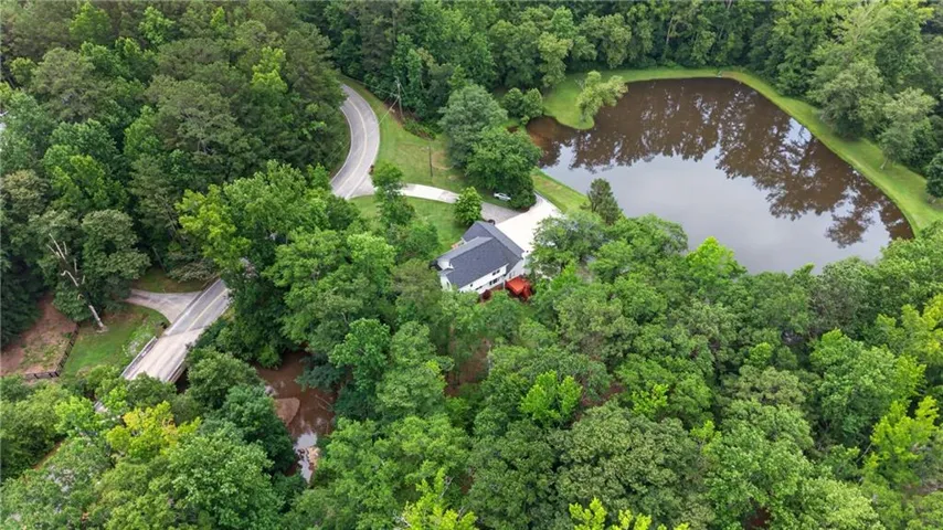Expansive wooded property featuring a private pond, a winding paved driveway, a detached residence with a dark-pitched roof, and a concrete bridge spanning a creek