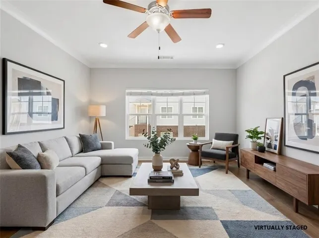 Spacious living area featuring crown molding, recessed lighting, wood-finish flooring, and a ceiling fan with integrated lighting