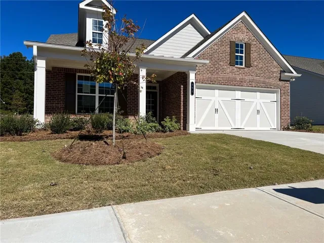 Brick exterior with white trim, covered front porch, white garage door with decorative hardware, and a dormer window