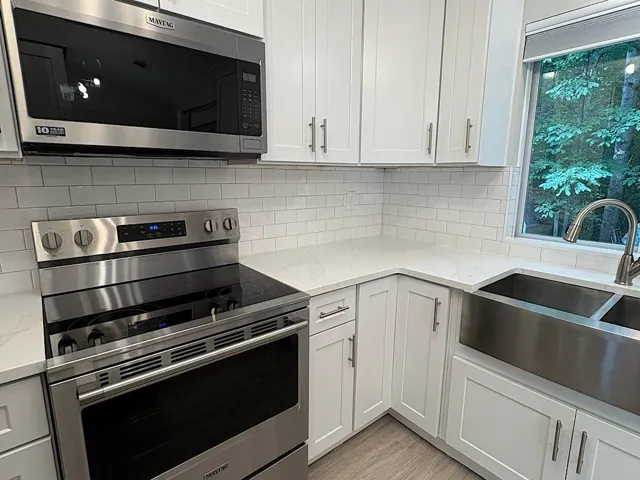 Stainless steel appliances, white cabinetry, a farmhouse-style sink, solid surface countertops, and subway tile backsplash