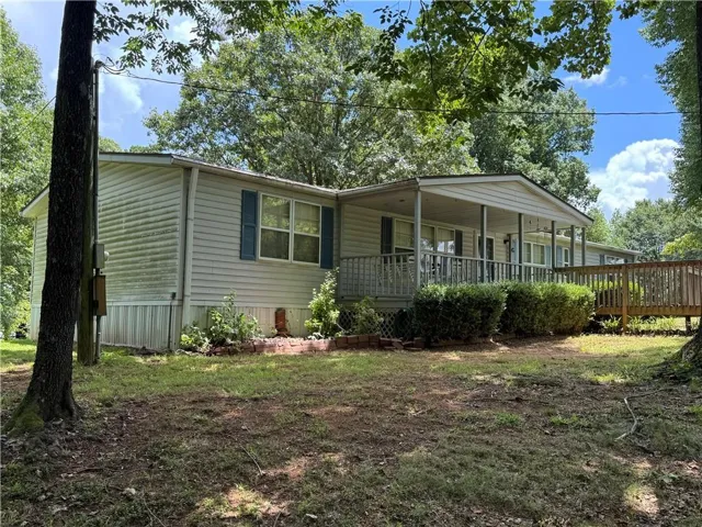 Ranch-style residence featuring a covered front porch, full-width wooden ramp, and mature trees providing natural shading