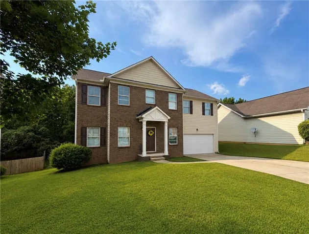 Brick and siding exterior with a covered entry, attached garage, paved driveway, and established front lawn