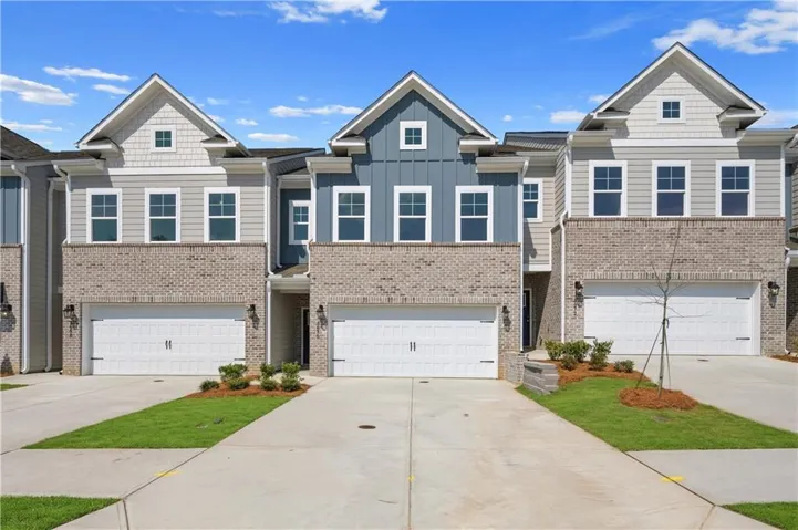 Modern townhomes featuring a combination of brick and siding exteriors, gabled roofs, two-car garages, and paved driveways