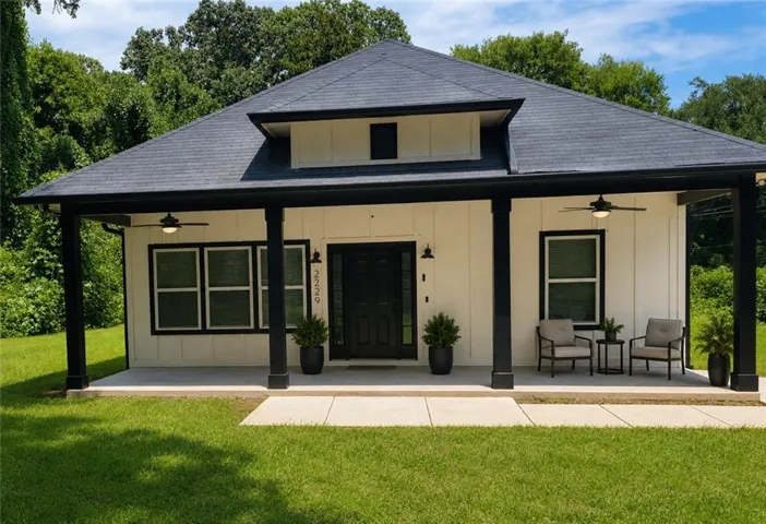 White board and batten exterior with a dark trim, covered porch with recessed lighting, dark asphalt shingle roof, and a dark front door (virtually staged)