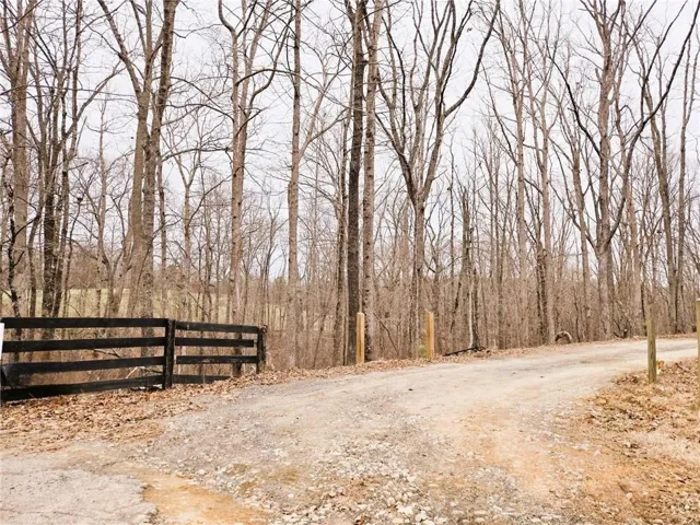 Gravel driveway with a black wood-panel fence and natural tree backdrop