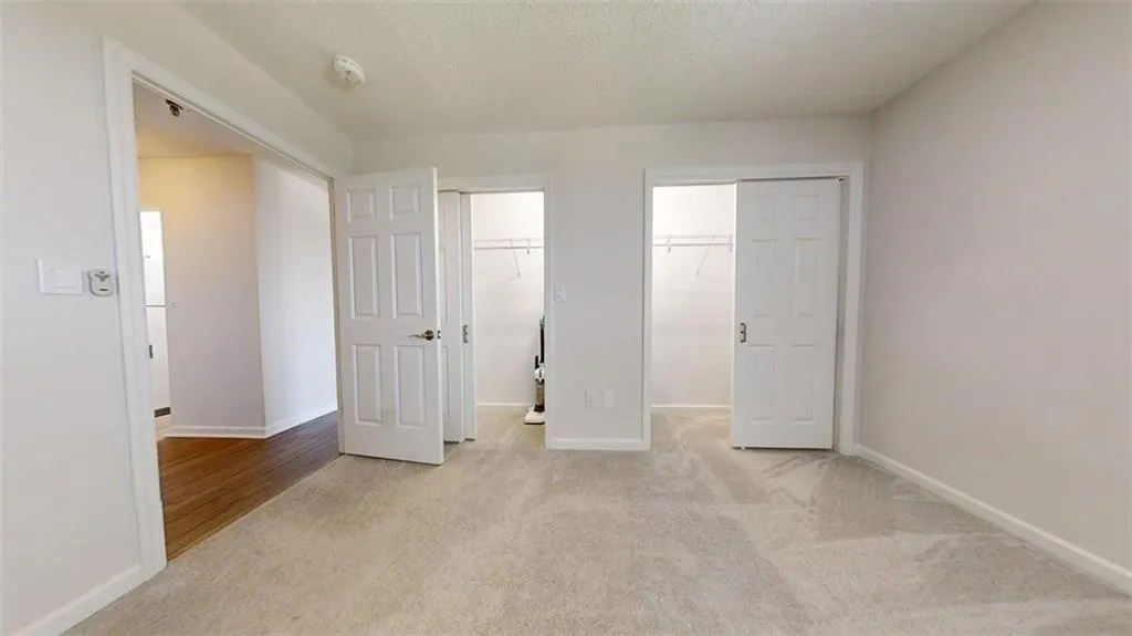 Unfurnished bedroom with light colored carpet, multiple closets, and a textured ceiling