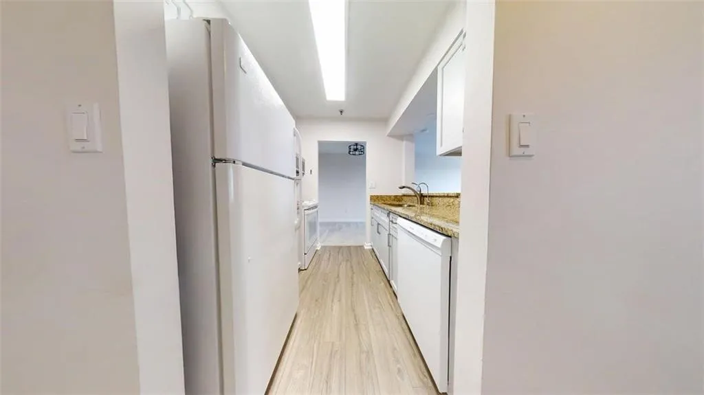 Kitchen featuring white appliances, white cabinets, light wood-style floors, and light stone counters